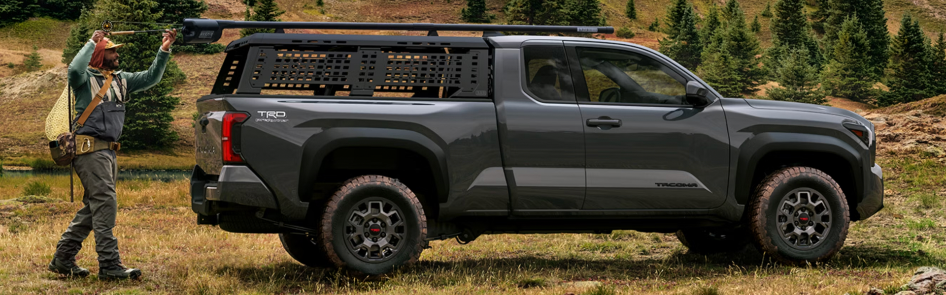 Side view of a 2026 Toyota Tacoma pickup truck driving off-road on grass.